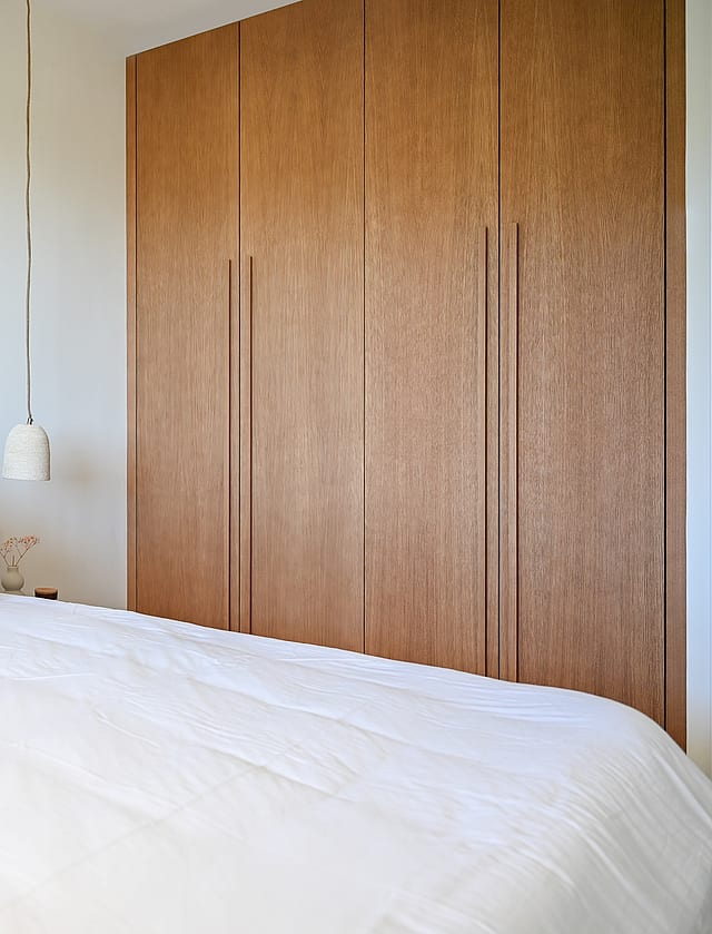 Guest bedroom with caramel linen bedding, oak low shelving beneath eaves, and minimalist Nordic styling