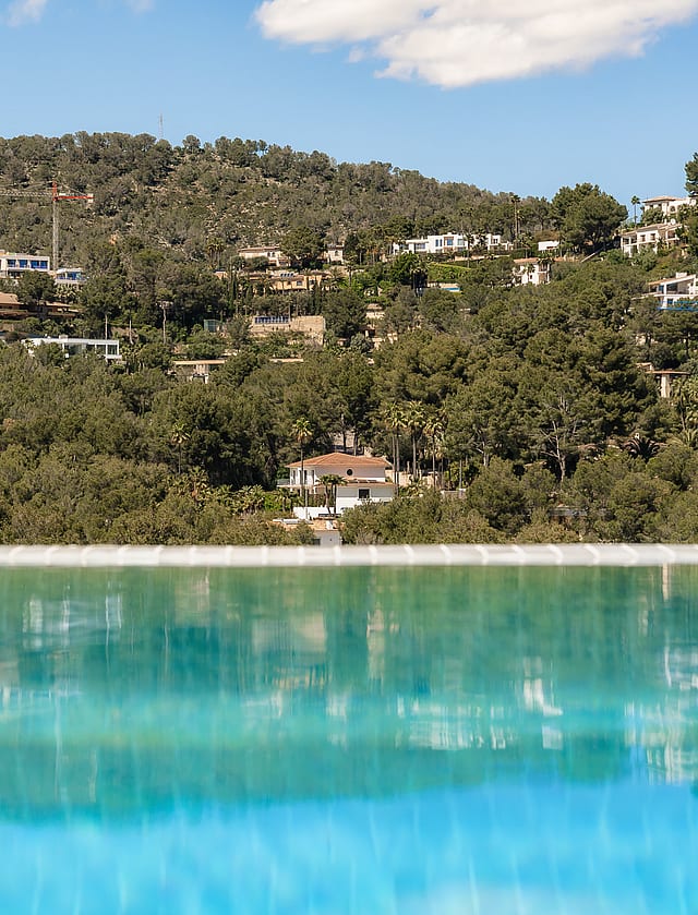Close-up of an infinity pool edge reflecting the lush green hillside and villas of Son Vida under a clear sky.