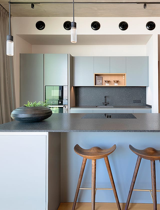 Contemporary kitchen featuring a grey island, dark stone countertops, wooden bar stools, and track lighting in a penthouse.