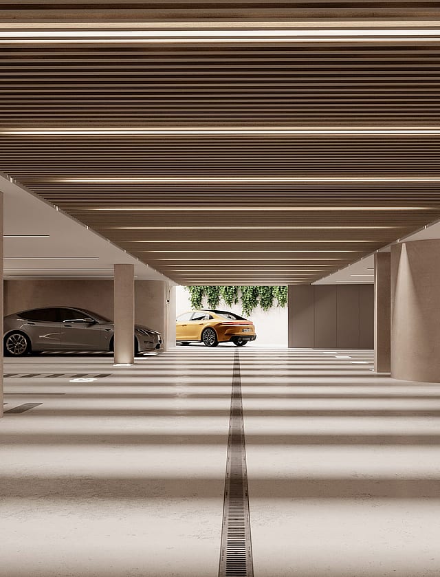 A modern, well-lit subterranean parking garage with concrete columns, linear ceiling lighting, and marked parking spaces.
