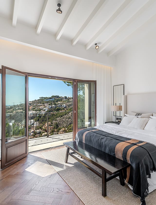Bright bedroom with herringbone wood floors and open French doors leading to a terrace with sweeping valley views.