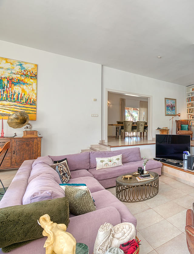 Spacious living room featuring a large lilac sectional sofa, a stone-fronted fireplace, and a light-colored tiled floor.