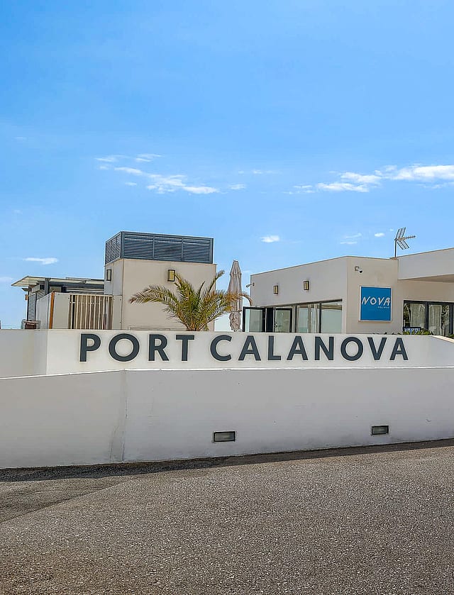 Exterior view of the white facade and entrance signage for Port Calanova under a clear blue sky.