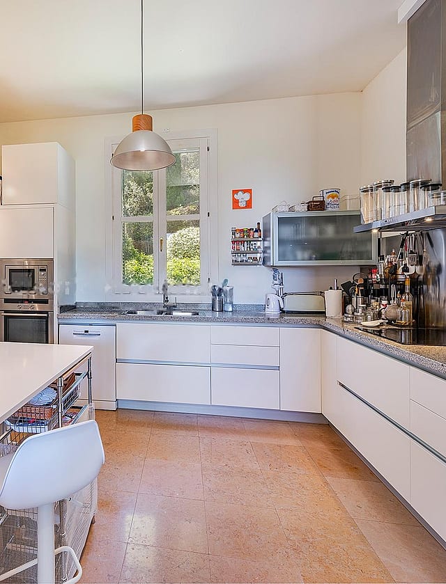 Contemporary white kitchen with stainless-steel appliances, island workstation, and glass doors opening to terrace