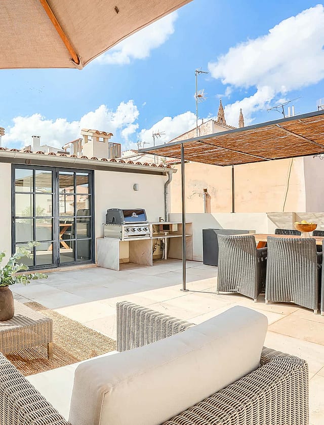 A spacious rooftop terrace in an Old Town townhouse features wicker seating, a dining area, and a built-in outdoor kitchen.