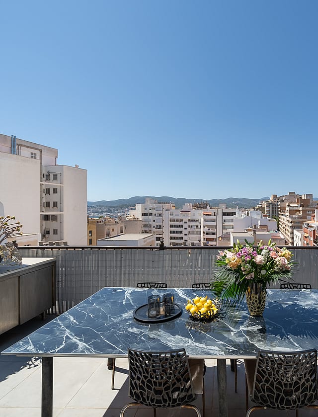 Outdoor dining table with marble top on a rooftop terrace overlooking Old Town buildings under a clear blue sky.
