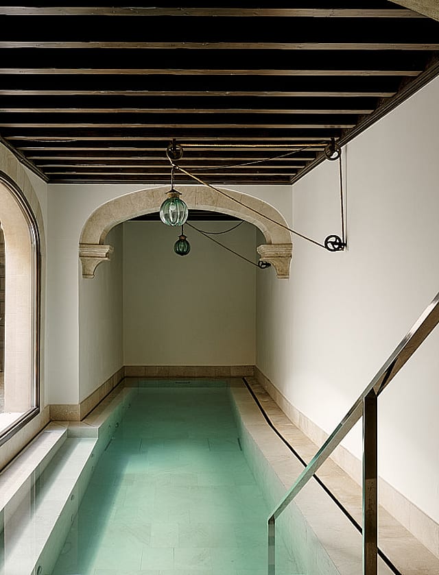 Indoor swimming pool featuring turquoise water, arched stone vault ceiling detail, minimalist contemporary design, and soft natural light