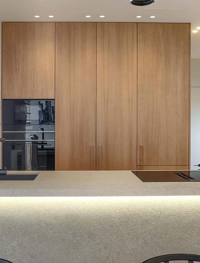 Modern kitchen with full-height oak cabinetry, a light stone kitchen island with integrated LED lighting, and built-in oven.
