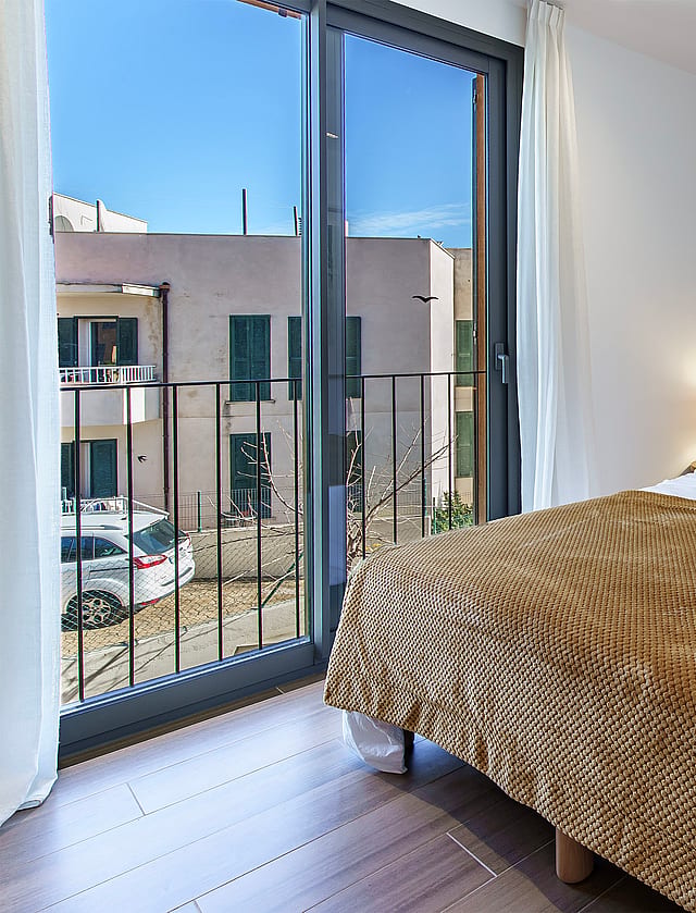 A contemporary bedroom with a double bed, brown patterned throw, and a sliding glass door opening to a small balcony.