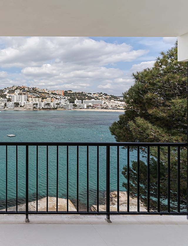 A balcony with black metal railing overlooking a turquoise bay and white coastal town under a soft sky.