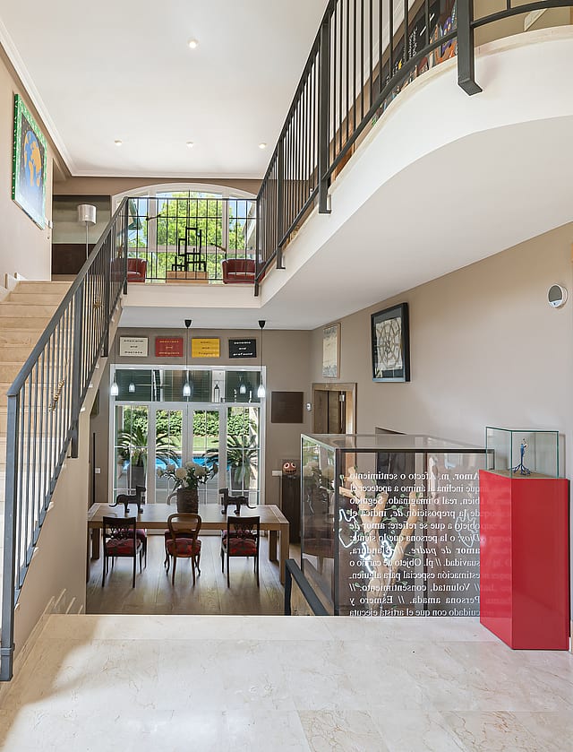 An expansive entrance hall with a polished stone staircase and ornate metal railings, looking towards a dining area beyond.
