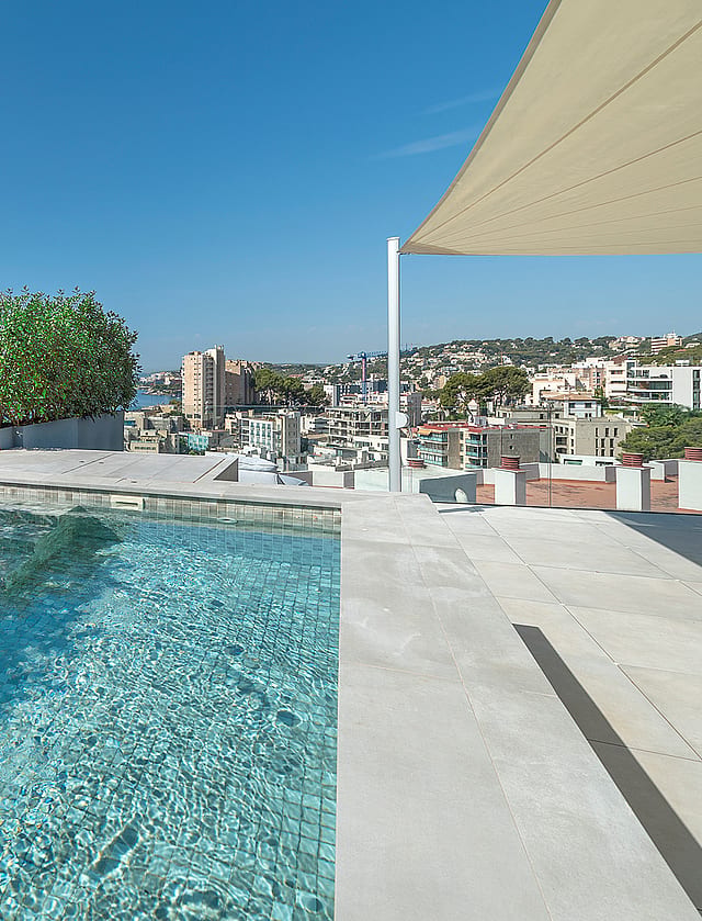 A private rooftop plunge pool with light blue tiled interior, framed by green shrubs, overlooking the Mediterranean sea.
