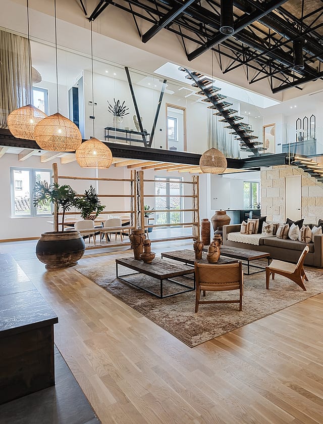 Double-height living space with light wood floors, a natural stone feature wall, and a dramatic steel staircase.