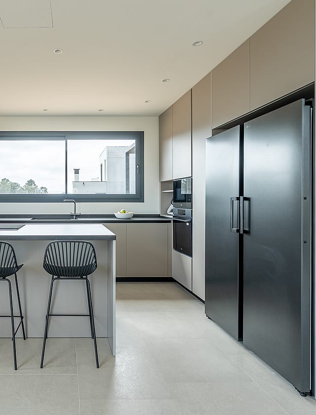 Modern open kitchen with light grey cabinetry, black refrigerator, and a central island with four black wire stools.