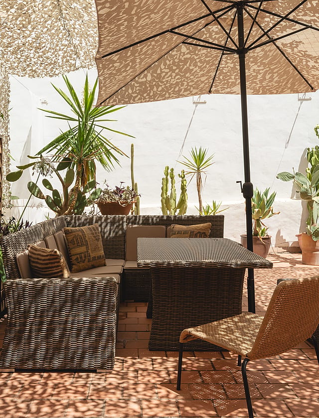 Outdoor terrace in Santa Catalina featuring woven lounge furniture, a large umbrella, and various potted cacti and plants.