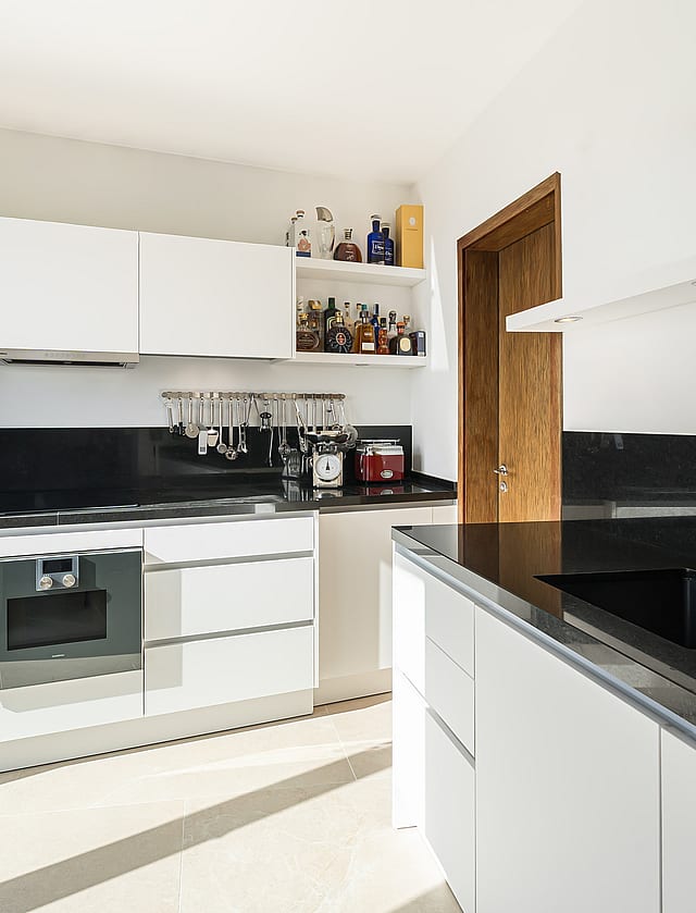 Bright modern kitchen with white handleless cabinets, black granite worktops, and stainless steel Gaggenau appliances.