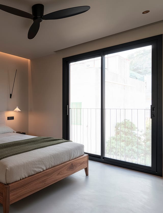 Minimalist bedroom featuring a wooden bed frame, floor-to-ceiling glass doors, and recessed ceiling lighting.