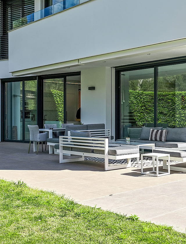 Rear of the villa with covered terrace, outdoor lounge seating and landscaped lawn.
