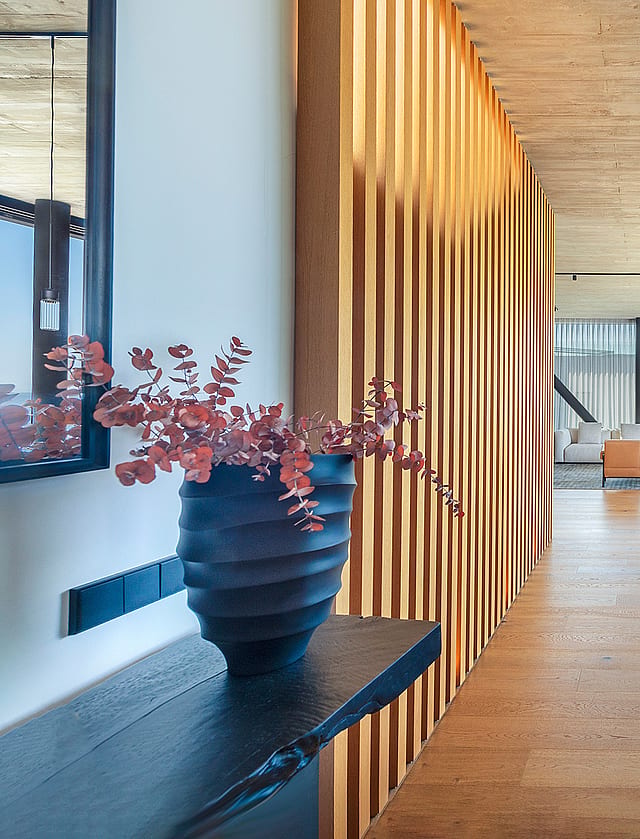 Interior of a modern kitchen showing a textured wood slat wall divider, dark kitchen island, and open-plan living area with horizon sea views.