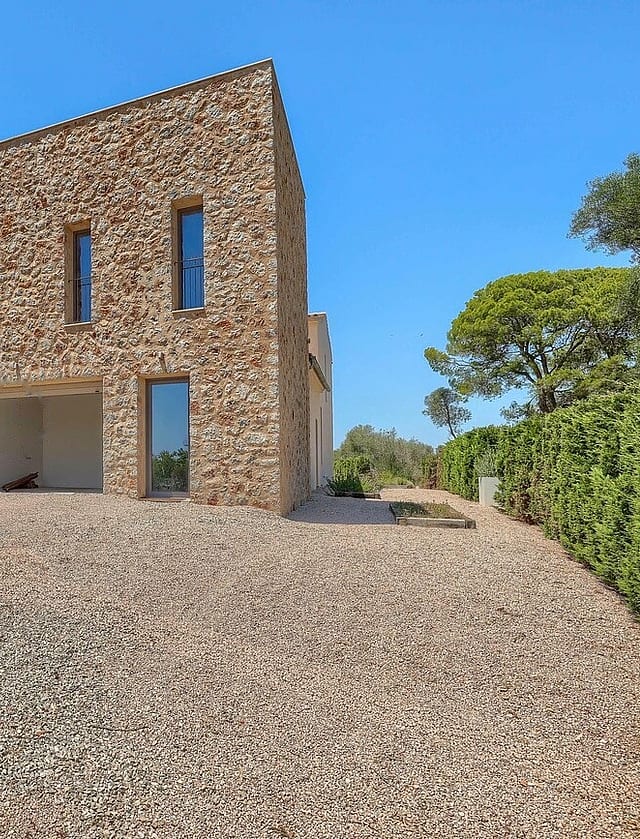 Two-story stone-clad outbuilding with narrow windows and an open ground-level portico, set against a gravel driveway.