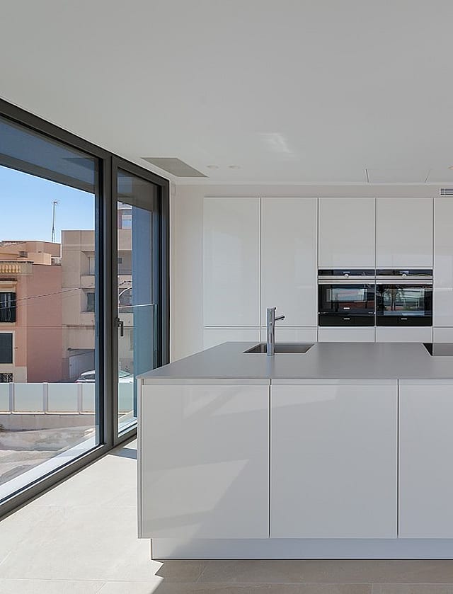Integrated white kitchen and living area with large sliding glass doors opening to terrace and sea view