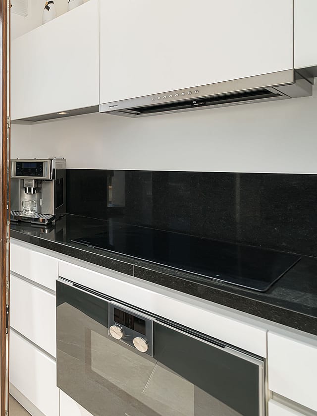 Modern white kitchen with black countertops opening to a sunny terrace with historic church views in Palma Old Town.