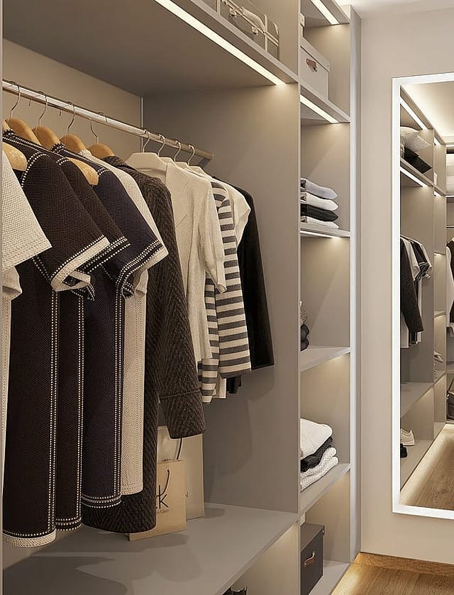 A modern walk-in wardrobe featuring hanging rails, open shelving, and a full-length mirror with LED perimeter lighting.