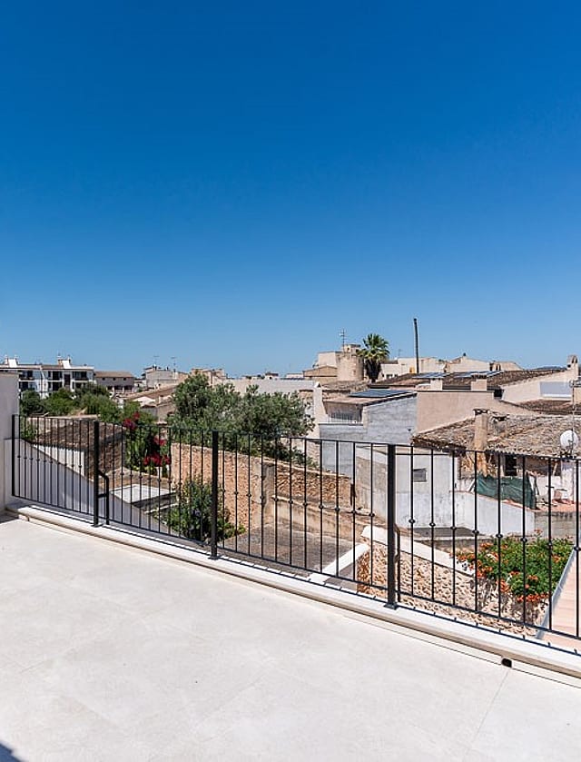 An open, paved rooftop terrace with white walls and a black metal railing overlooking the traditional tiled roofs of Campos.