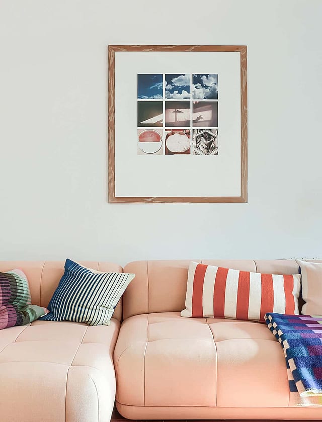 A pale pink sectional sofa sits against a plain white wall, decorated with colorful cushions and a grid-style framed print.