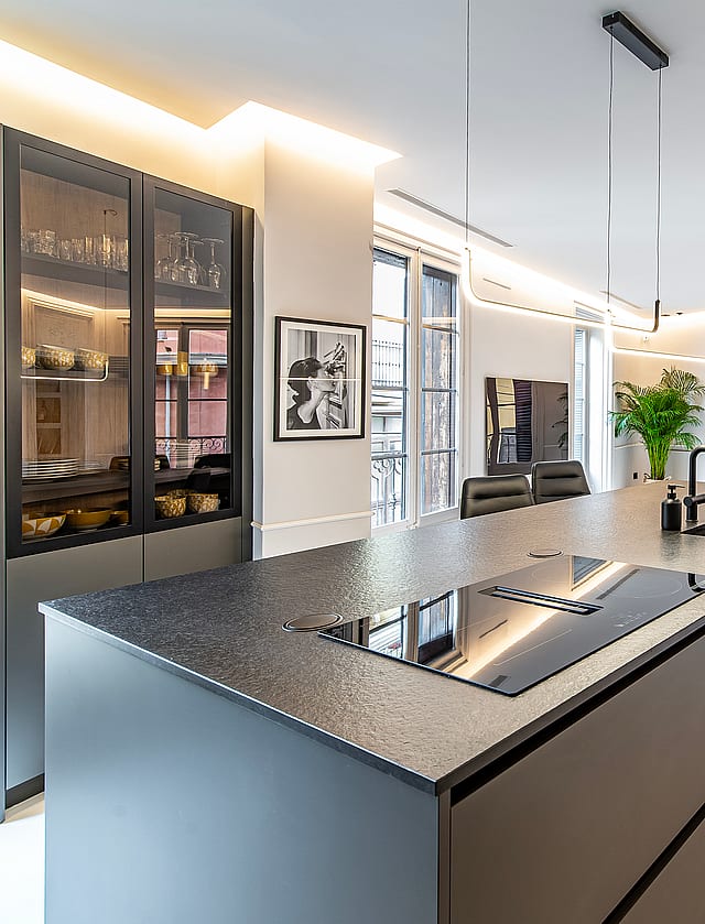 Modern open-plan kitchen with a large dark charcoal island, integrated appliances, and recessed lighting, overlooking a bright living area.