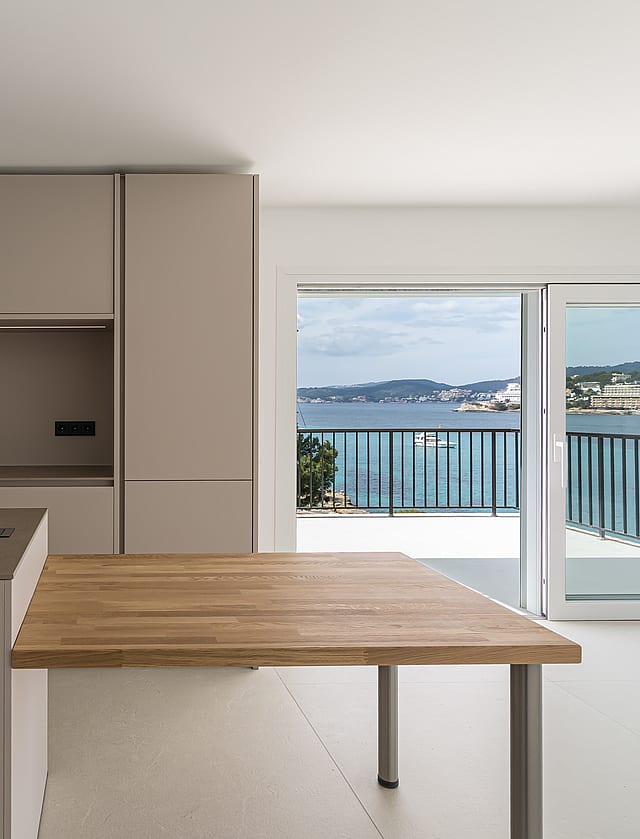 Minimalist kitchen with taupe cabinetry and an oak dining surface opening onto a sea-view terrace.