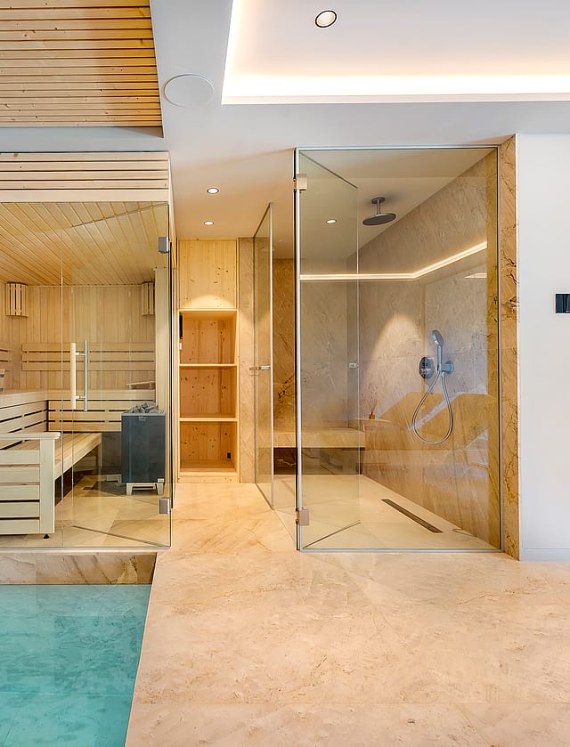 Modern home spa featuring a glass-enclosed cedar sauna beside a walk-in rainfall shower with stone flooring.