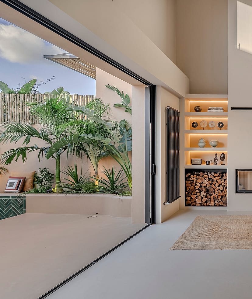 Double-height living area featuring a built-in sofa, modern fireplace, and glass doors opening to a tropical patio.