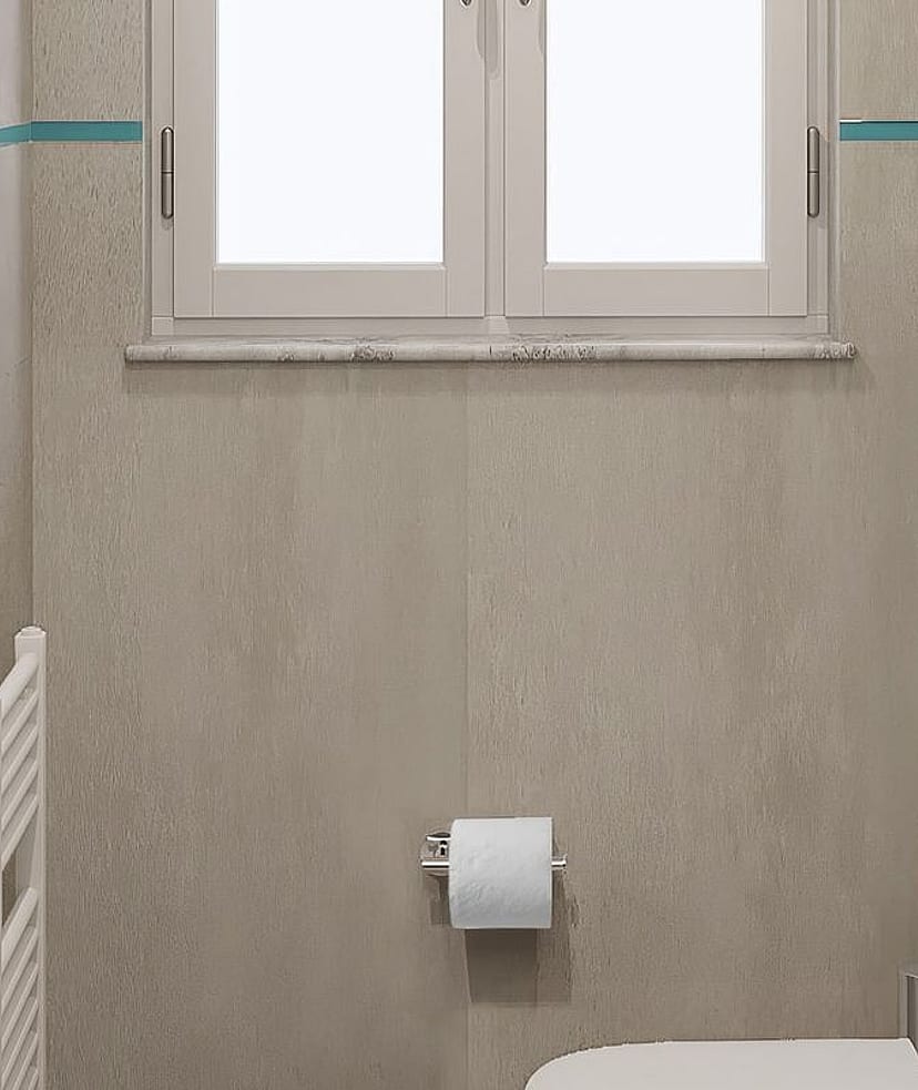 Interior view of a minimalist bathroom featuring grey stone tiles, a white wall-mounted toilet, and a small window.