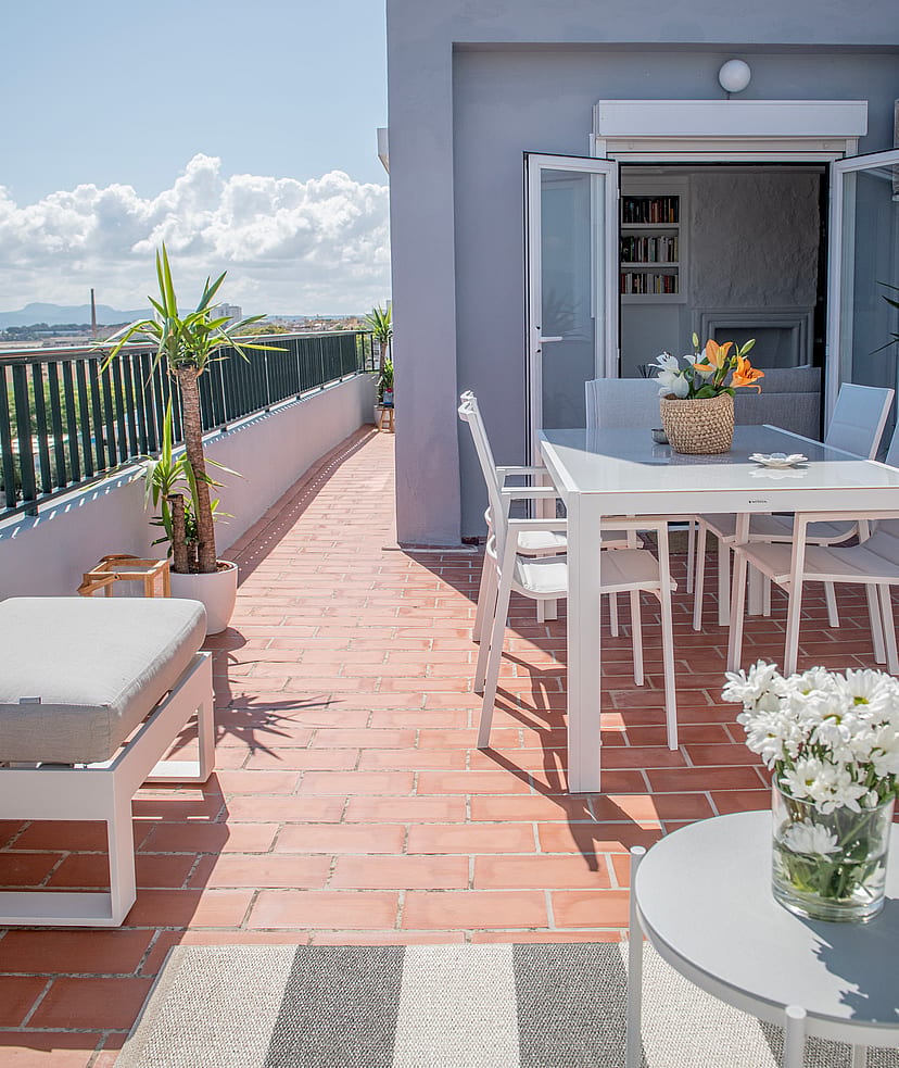 A sunlit rooftop terrace in El Molinar with a white dining set, terracotta tiles, and mountain views in the background.
