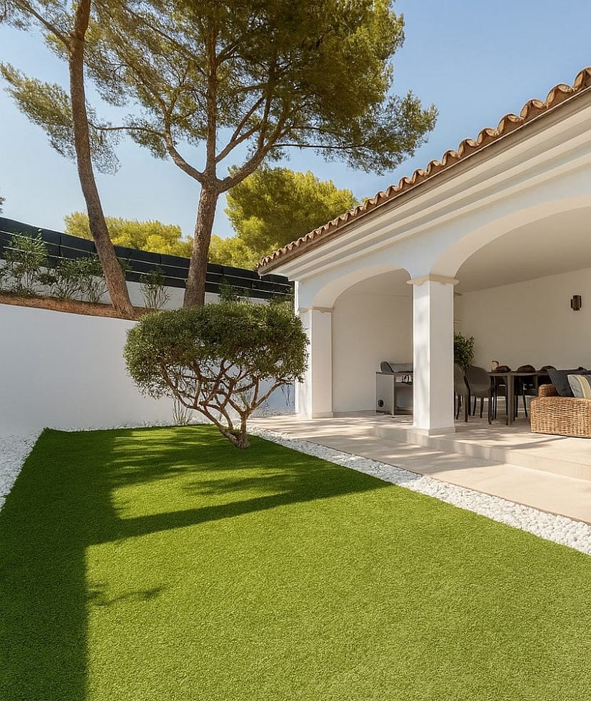 Covered outdoor terrace with white arched columns, dining table and wicker sofa opening onto lawn and mature pines