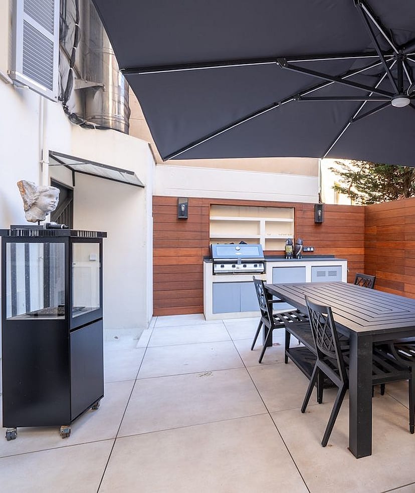 A private outdoor terrace in Palma featuring a dining table, black chairs, a large charcoal umbrella, and a built-in grill.