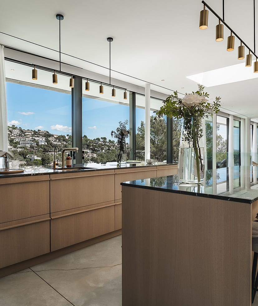 Contemporary kitchen featuring a wooden island with bar seating, dark countertops, and windows overlooking green hills.