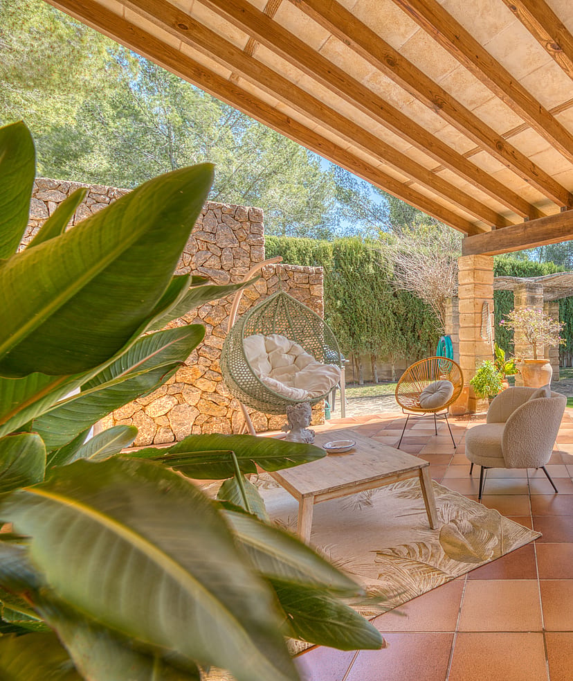 A covered terrace with terracotta floor tiles and wooden beam ceiling, featuring outdoor armchairs and a dry stone wall.