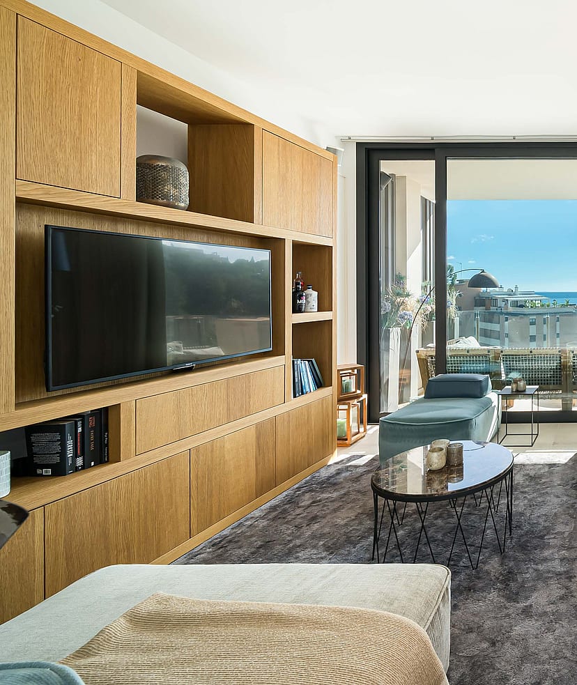 Modern living room featuring floor-to-ceiling oak cabinetry, neutral upholstered seating, and sliding glass doors to a terrace.