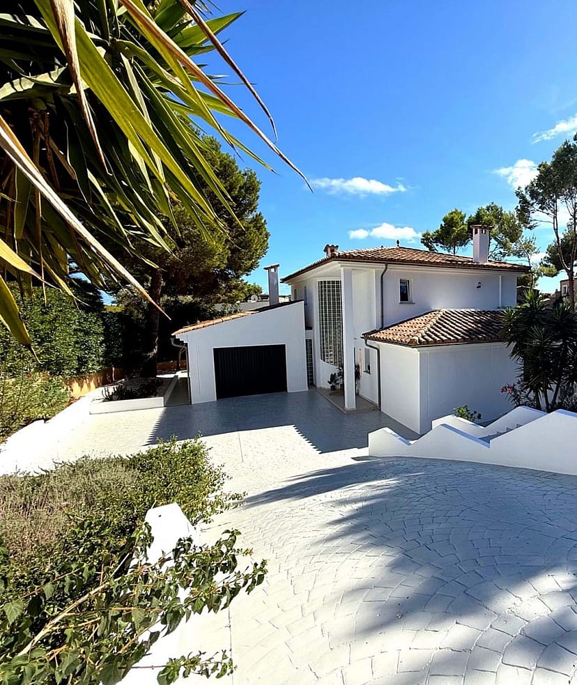 Front elevation of a white two-storey villa with terracotta roof, double garage and wide paved driveway