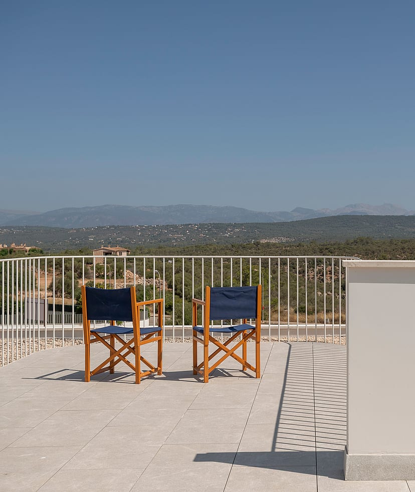 Elevated stone terrace with two wooden chairs facing a mountain landscape under a clear blue sky.