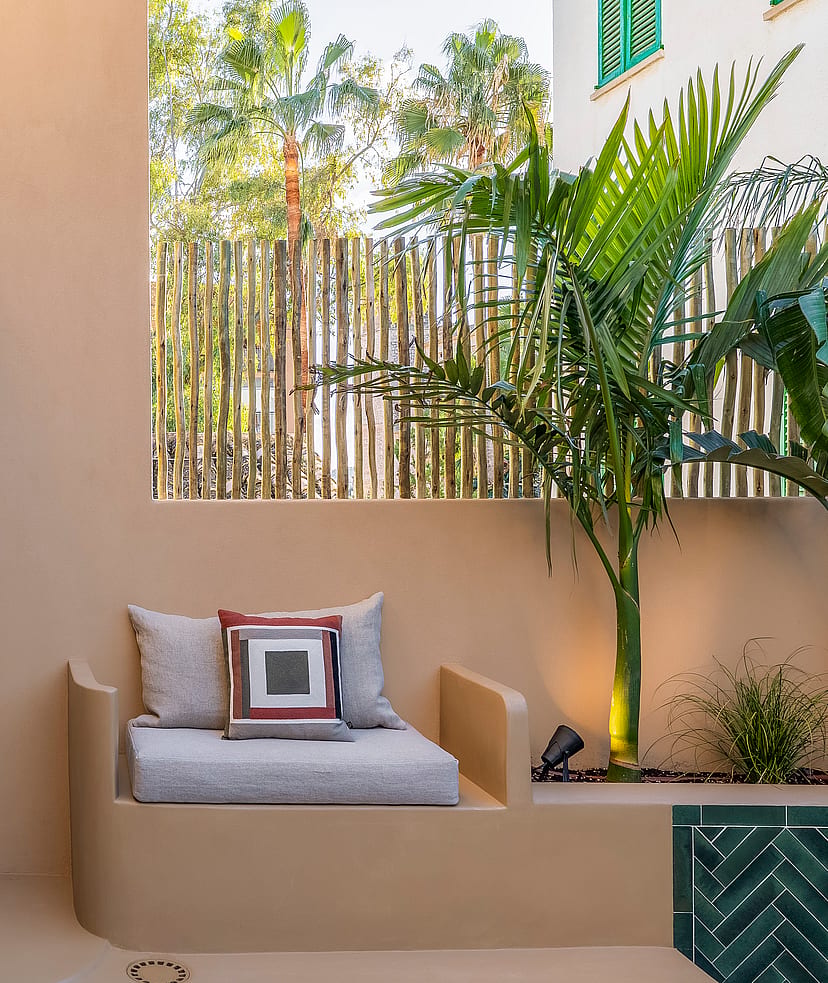 Modern outdoor shower with black fixtures next to a built-in masonry bench and tropical plants.