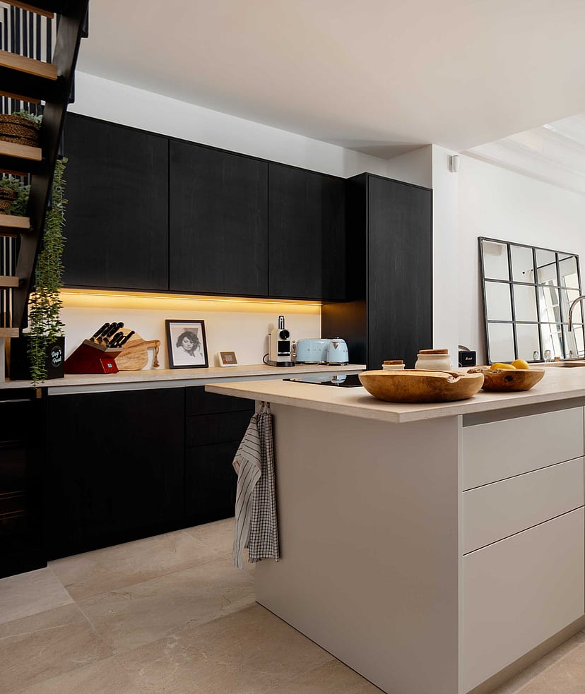 Open kitchen with black cabinetry, a pale stone-topped island, and a dining table and French doors visible beyond.