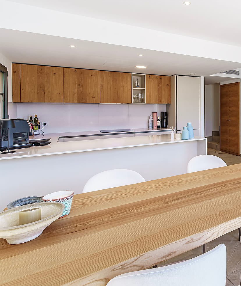 A bright open-plan space showing a kitchen with wooden cabinetry, a breakfast bar, and a living area featuring a stone wall.