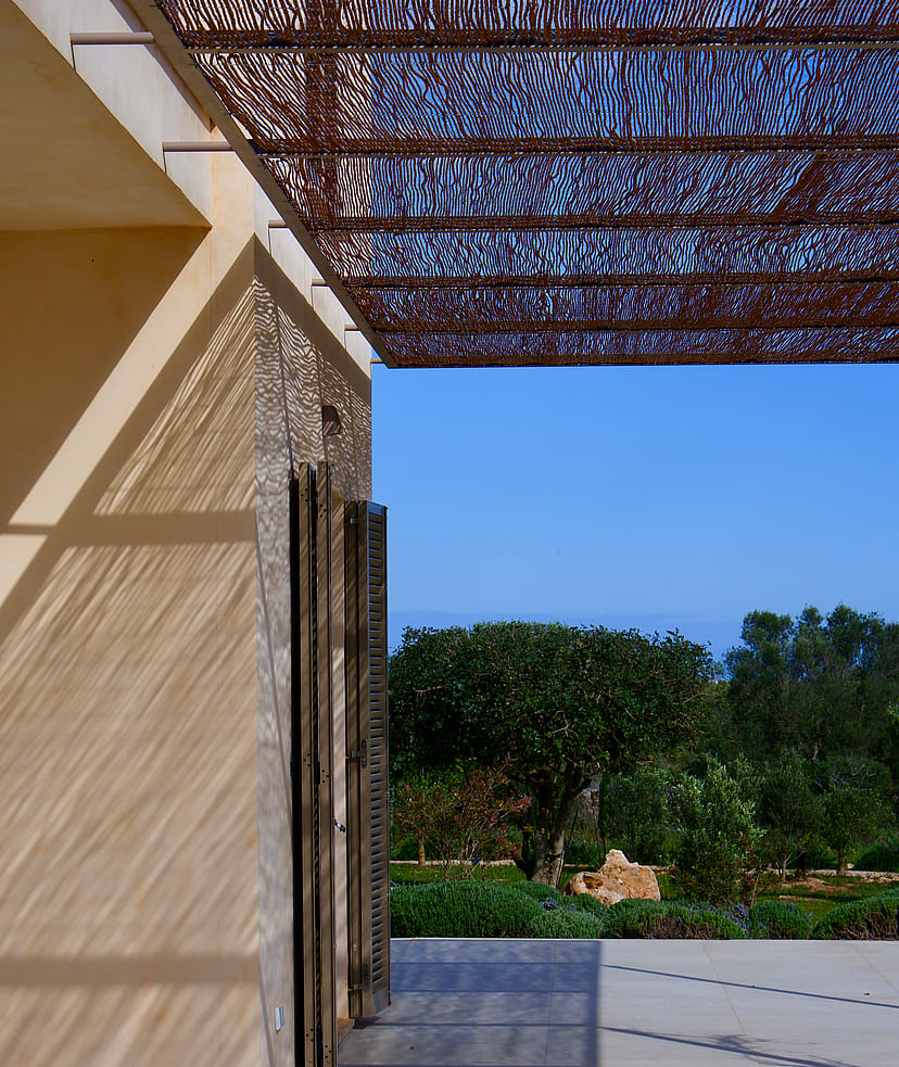 A modern outdoor terrace in Santanyí featuring a geometric laser-cut metal pergola casting intricate shadows on stone walls.