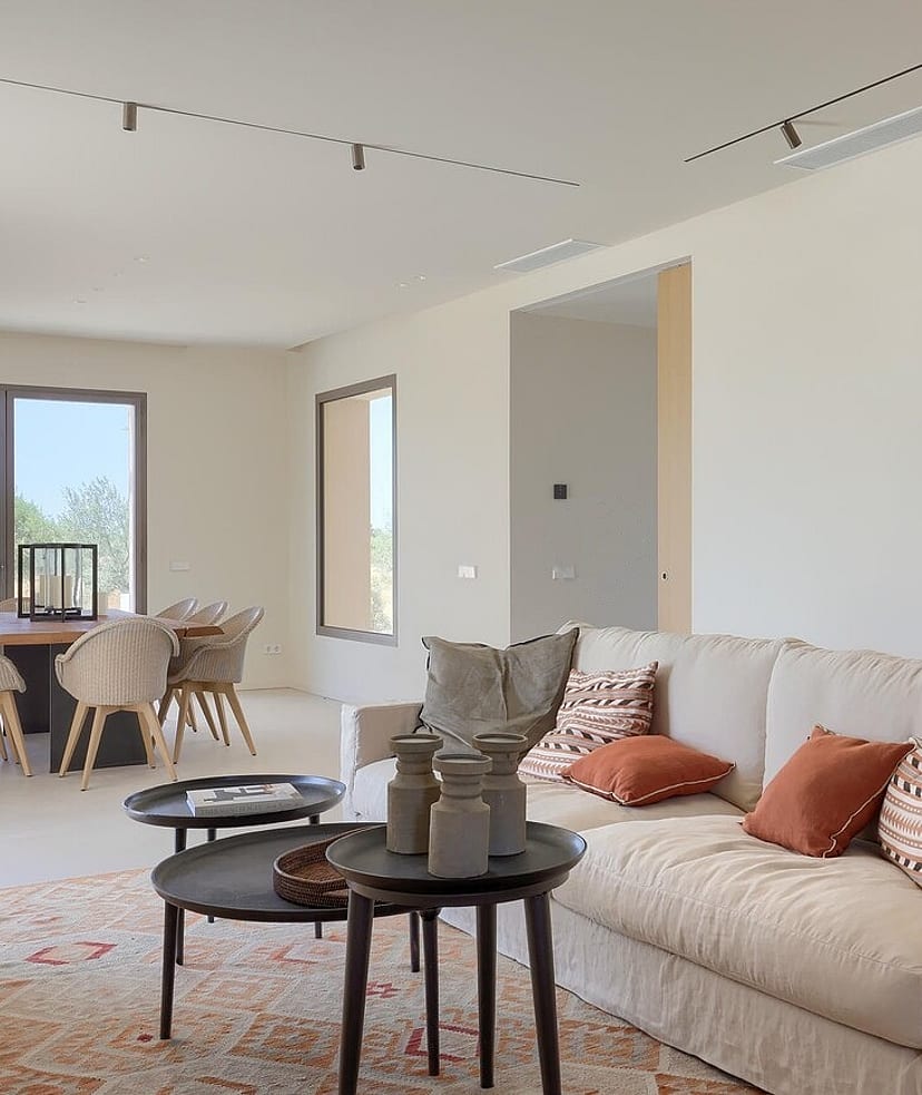 An open-concept living and dining space with a cream fabric sofa, nested coffee tables, and a wooden dining set near a large window.