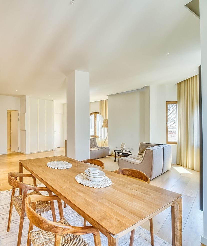 Open-plan room featuring a light wood dining table with curved wooden chairs and a minimalist kitchen island with bar stools.