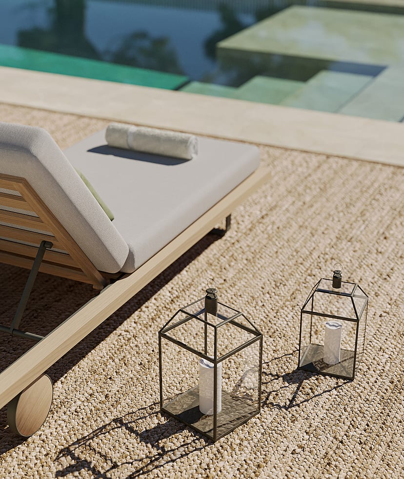 Close-up of a wooden sun lounger with cream cushions beside a pool, with two decorative metal lanterns on a gravel terrace.