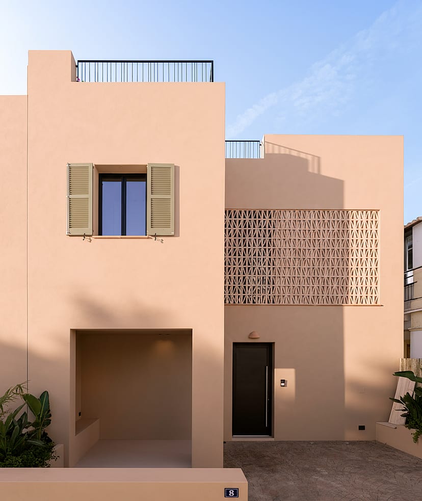 Front view of a two-story beige townhouse in Genova with geometric terracotta latticework and a covered entrance alcove.